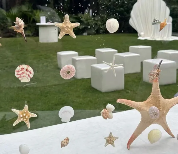 White shells and starfish on clear acrylic, with white cube seats and a giant shell on a lawn
